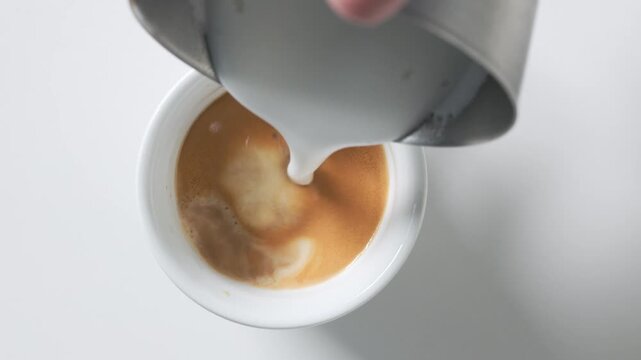 Top view of a rotating cup of freshly brewed espresso on a white background as steamed milk is poured in to create a creamy cappuccino