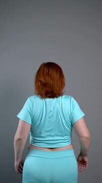 Unrecognizable curvy woman performs exercises for muscles of upper back and shoulder joint, posture correction and physical therapy concept on gray background