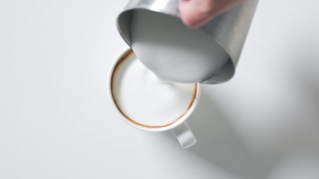 Top view of a rotating cup of freshly brewed coffee on a white background as steamed milk is poured in to create a creamy cappuccino