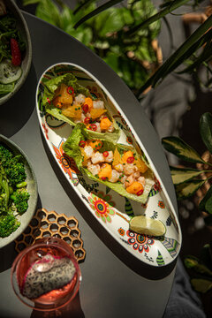 Healthy summer salad with prawns avocado cucumber and strawberry served on table with tropical green leaves shadows