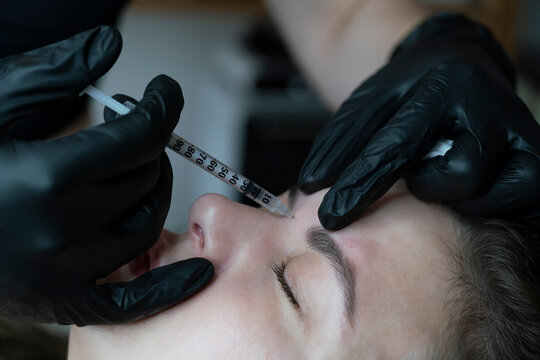 woman lies in an armchair, receiving a cosmetic injection, a close-up of a rejuvenating injection in the forehead