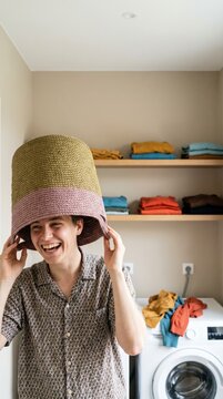 Playful young person balancing a laundry basket on their head in a utility room
