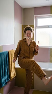 Woman in striped pajamas brushing her teeth playfully in a colorful bathroom