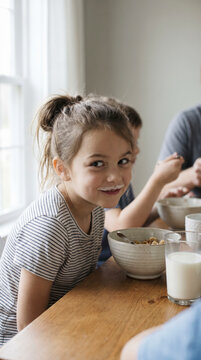 Young girl with a milk moustache smiling brightly at a family breakfast table