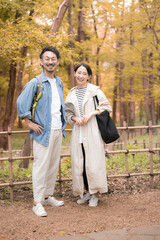 Fototapeta premium 紅葉の中でカメラ目線の笑顔を見せる日本人カップル 秋の旅行・観光のレジャーお出かけイメージ全身