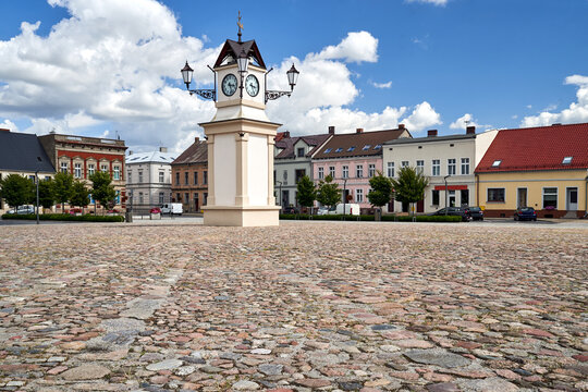 A cobblestone market square surrounded by tenement houses with a clock tower in Lw&oacute;wek