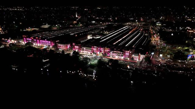 Panoramic night aerial drone video of illuminated Howrah Junction railway station in Kolkata with glowing lights, showcasing historic railway architecture, tracks, and Hooghly riverbank.