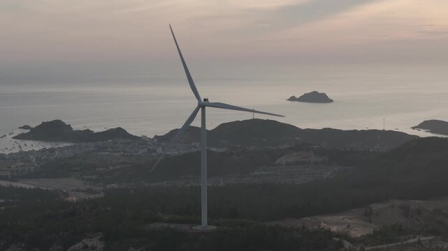 Aerial drone footage of sunrise over Ky Mountain Wind Farm near Quy Nhon, Gia Lai, Vietnam, featuring coastal scenery, wind turbines, golden morning light and renewable energy.