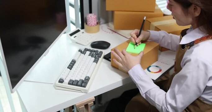 Warehouse employee processing inventory, checking shipping documents, updating stock records, and managing parcel information at an office workstation for logistics and warehouse operations.
