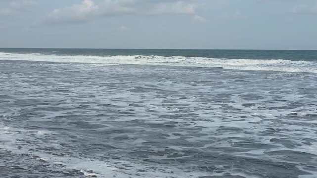 Plastic trash and debris scattered on a dark sand beach with ocean waves of the Indian Ocean during late afternoon, environmental pollution and ocean conservation concept.