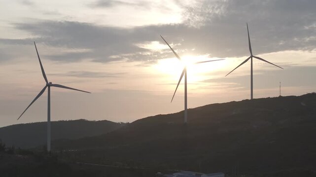 Aerial drone footage of sunrise over Ky Mountain Wind Farm near Quy Nhon, Gia Lai, Vietnam, featuring coastal scenery, wind turbines, golden morning light and renewable energy.
