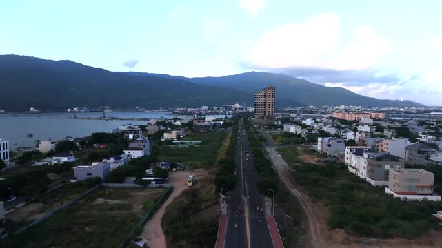 Smooth drone flight following a coastal road toward the mountains with urban scenery in Da Nang, Vietnam.