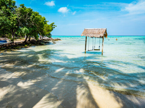 Scenic Barakuda Beach with a rustic wooden swing set over clear shallow turquoise water next to lush green trees, creating a relaxing holiday getaway scene in Karimunjawa, Indonesia