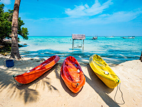 Three vibrant kayaks are waiting on the sandy shore of Barakuda Beach, Karimunjawa, Indonesia, inviting tourists to enjoy water sports and tropical island relaxation under a clear blue sky