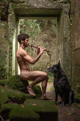 Man playing ancestral flute in an abandoned temple next to a black dog © Nander PS