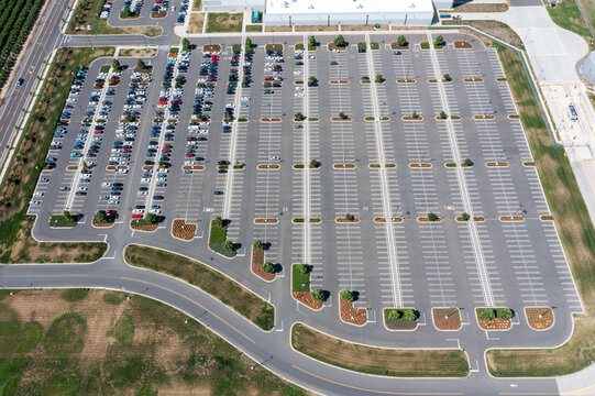 Aerial drone photo of a large commercial parking lot with parked cars beside an industrial warehouse and distribution facility in Woodburn, Oregon, USA on a clear summer day