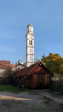 Wooden barn, tall clock tower of Monastery of Saint Basil of Ostrog in background. Bijeljina (Бијељина), Bosnia and Herzegovina.