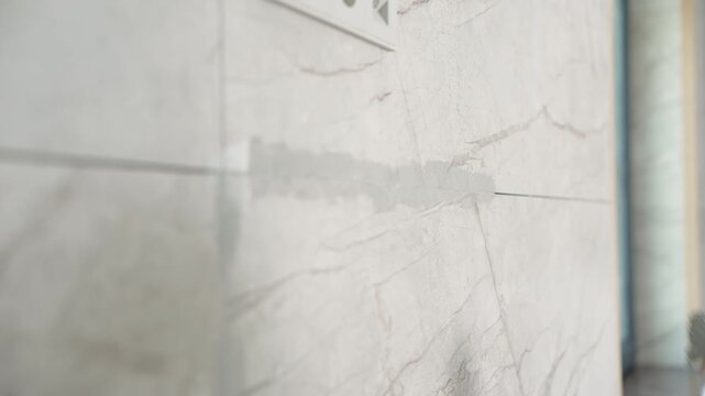 Applying epoxy grout by hand between large format white ceramic tiles using a blue trowel.