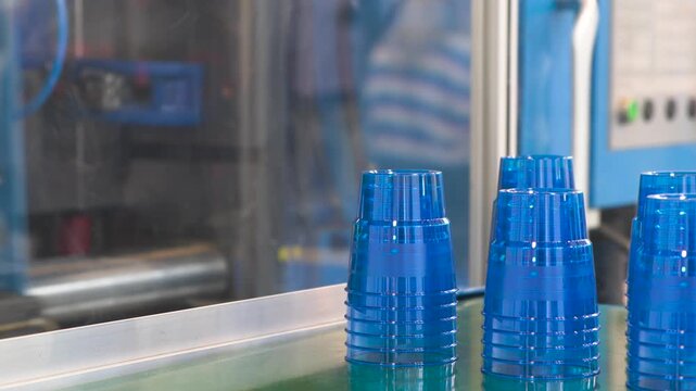 machine is making plastic cups. cups are blue and are lined up on conveyor belt