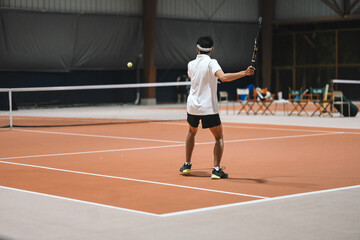 Obraz premium Male Tennis Player Hitting Ball on Indoor Clay Court During Training Session