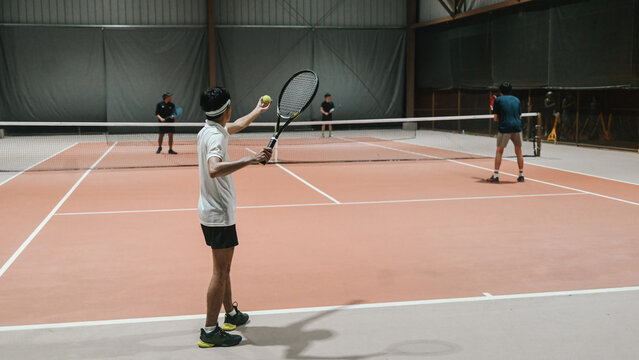 Men Playing Doubles Tennis Match on Indoor Clay Court with Racket and Ball Ready to Serve