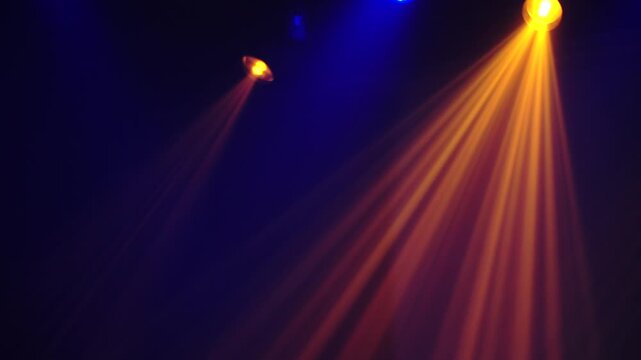 Bright theatrical spotlights shining through atmospheric haze, dynamically changing colors from crisp white to warm orange in a dark event venue.