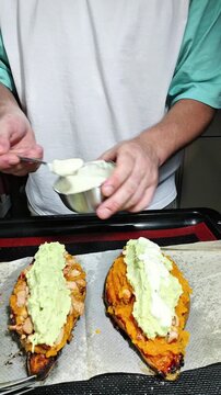 Adding creamy sauce onto roasted sweet potatoes for healthy homemade dinner preparation today