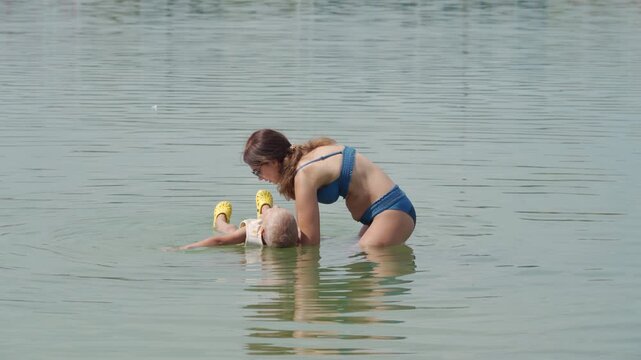 A loving mother gently cradles her trusting son as he floats. They share a peaceful, calm moment in a warm lake filled with green algae.