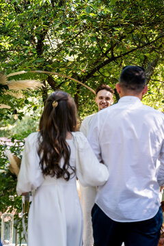 Joyful groom smiles at bride and officiant during outdoor wedding ceremony