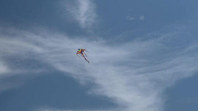 Colorful kite flying high in blue sky with wispy clouds