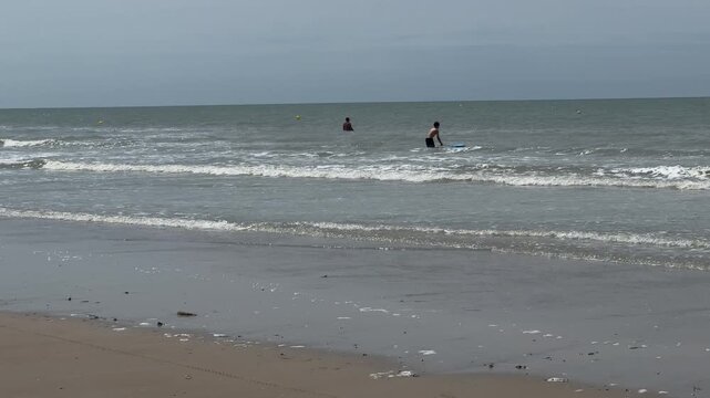 People swimming in shallow sea waves on overcast beach