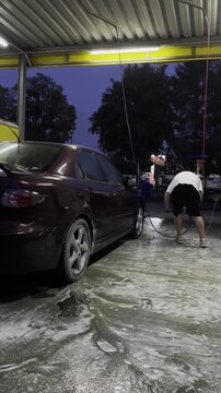 Man Washing Black Car at Self Service Car Wash Using High Pressure Water Jet, Cleaning Vehicle Exterior at Outdoor Washing Station, Automotive Maintenance, Car Care Routine, Transportation Lifestyle V