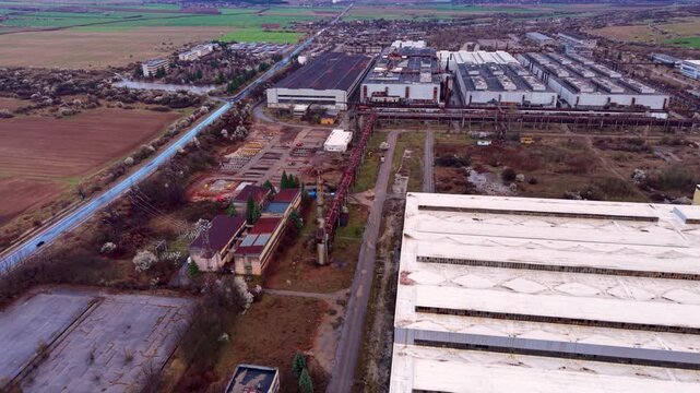 Aerial view of an abandoned or inactive industrial facility with large rooftop ventilation stacks, weathered concrete structures and overgrown grounds, showing aging infrastructure and industrial deca