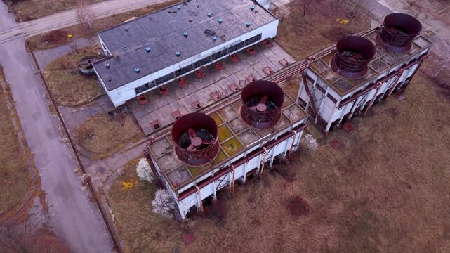 Aerial view of an abandoned or inactive industrial facility with large rooftop ventilation stacks, weathered concrete structures and overgrown grounds, showing aging infrastructure and industrial deca