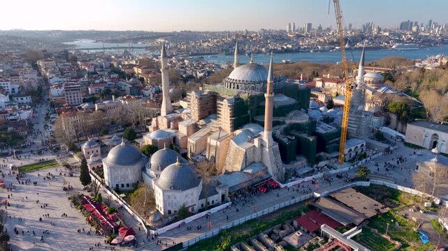 Spectacular aerial drone view of the Blue Mosque (Sultan Ahmed Mosque) in Istanbul, Turkey, with Hagia Sophia, the Bosphorus, and the modern city skyline in the background. Golden hour lighting highli