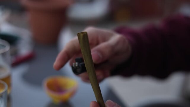 Close-up view of hands lighting up a cannabis cigarillo, preparing to smoke recreational marijuana
