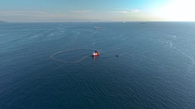 Top-down aerial view of a commercial fishing vessel deploying a large circular purse seine net across deep blue sea, enclosing a wide area of water during an active fishing operation.