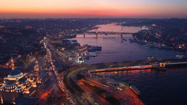 Cinematic aerial panorama of the Golden Horn during sunset in Istanbul, Turkey. Ferries navigate the water beneath the illuminated Atat&uuml;rk Bridge while the historic waterfront and city skyline glow du