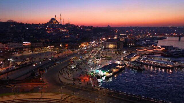 Cinematic aerial view of the illuminated S&uuml;leymaniye Mosque during sunset in Istanbul, Turkey. The iconic Ottoman landmark dominates the historic skyline while city lights emerge beneath a colorful tw