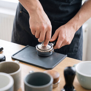 Barista's hands tamping espresso grounds with a stainless tamper on a clean tamping mat from above