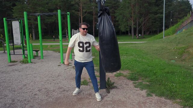Man in white jersey boxes black punching bag at outdoor park gym