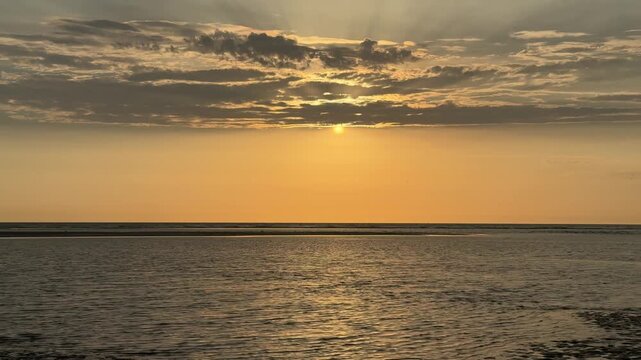 Golden sunset over calm sea beneath dramatic clouds