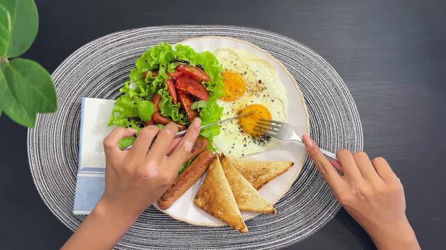 High angle footage of hand holding a fork and taking food from a breakfast plate. Concept of morning routine, eating process, tasty breakfast, food blog, morning meal, and lifestyle video. Real-time m