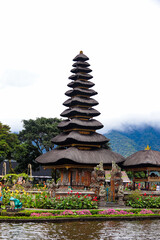 Obraz premium A close-up vertical shot of the multi-tiered roof meru tower at Ulun Danu Beratan Temple, bordered by vibrant pink flowers and foggy hills in Bali.