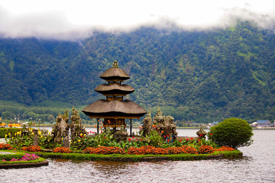 Iconic view of Pura Ulun Danu Beratan water temple on Lake Beratan, surrounded by colorful flower gardens and misty foggy mountains in Bedugul, Bali.
