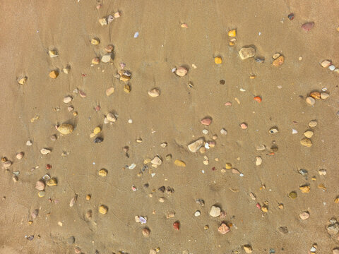 golden beach sand with colorful pebbles and small stones, natural coastal texture background, top view