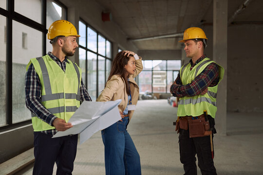 Displeased female architect arguing with manual workers over blueprint problems at construction site