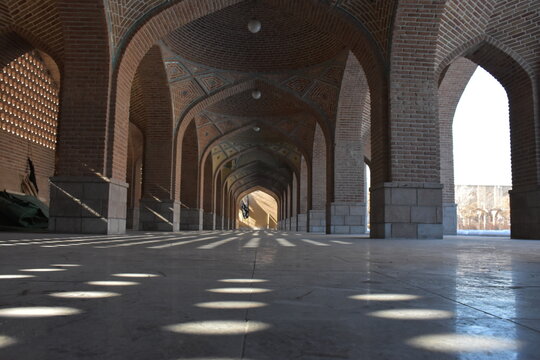 Low angle view of Blue Mosque interior in Tabriz Iran with repeated brick arches, geometric decoration and patterned sunlight