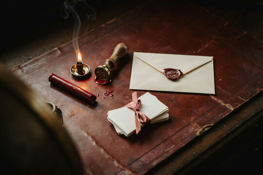Vintage wax seal and handwritten letter on antique wooden desk, red sealing wax, paper envelope with stamp, moody classic stationery still life