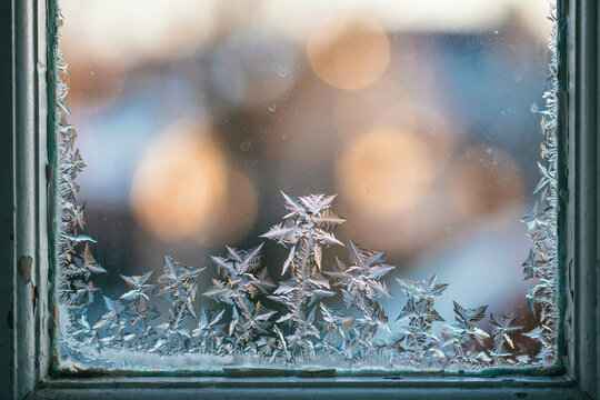 Icy window frame with frost and snowflake patterns, winter cold weather background with soft bokeh lights for seasonal design